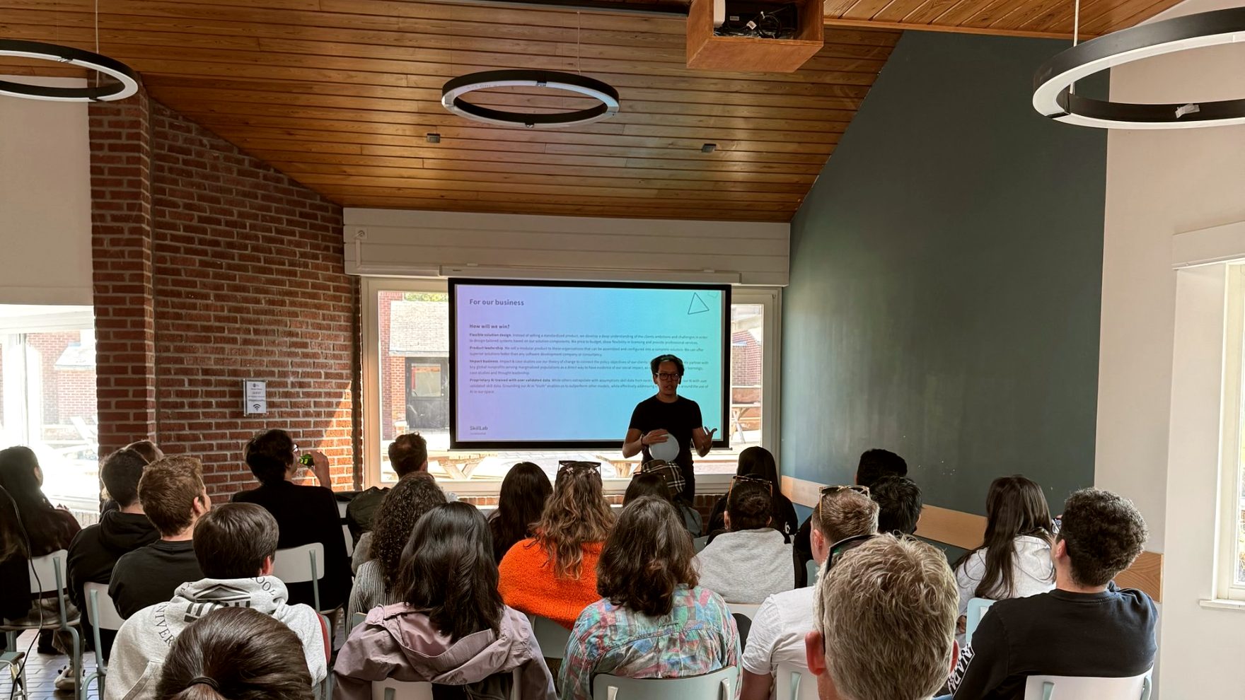 Arthur Chiba presenting to a seated group in a brick and wood room